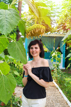Portrait of an adult woman off-the-shoulder clothing, on a sun-drenched alley among blooming yellow sunflowers and tall palm trees.