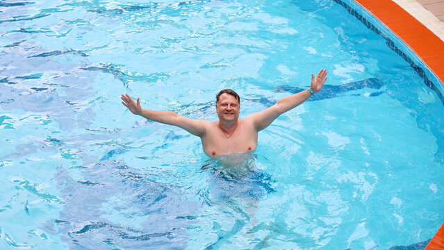 Happy adult man swimming and relaxing in his own private backyard swimming pool near a house on a sunny warm summer day.