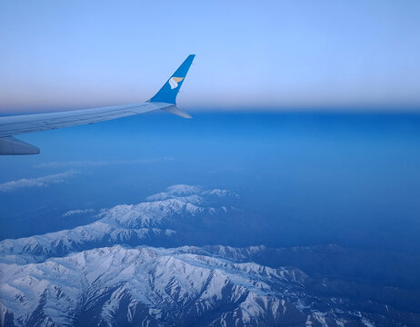 Oman Air flight from Moscow to Muscat, Oman - May 18, 2026: Snow capped mountains seen from the airplane window at sunrise on the way