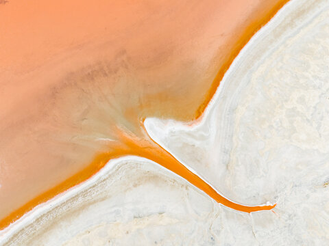Aerial view of the abstract patterns of a salt lake with vibrant orange water and white salt crust in the Mallee region, Woorinen North, Victoria, Australia.