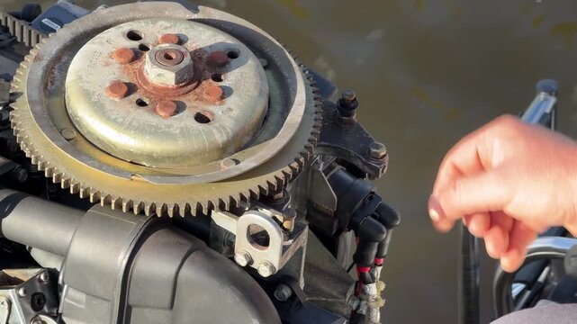 Close up of an open outboard boat motor exposing the flywheel and metal mechanical parts in bright natural daylight.