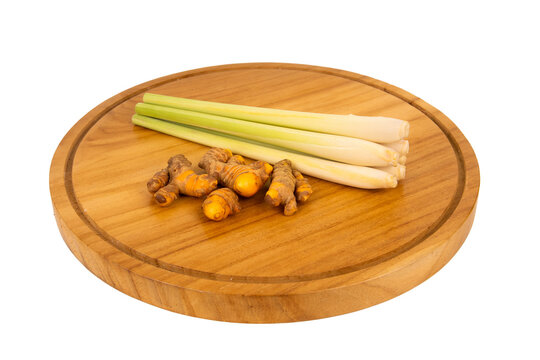 Fresh lemongrass stalks paired with raw turmeric roots on a wooden cutting board, isolated on white. High-quality spice ingredient stock photo for cooking.