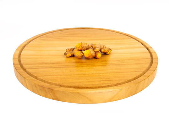 Fresh organic raw turmeric roots clustered on a round wooden cutting board, isolated on white background. Premium stock photo for culinary and wellness use.