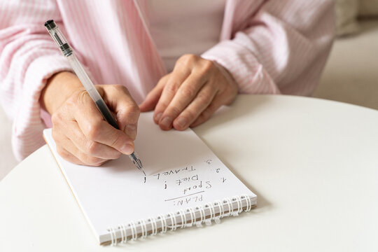 Woman at home writes down personal goals and plans regarding fitness, nutrition, and travel in notebook. A cozy home atmosphere reflecting slow living, mindful planning, and biohacking