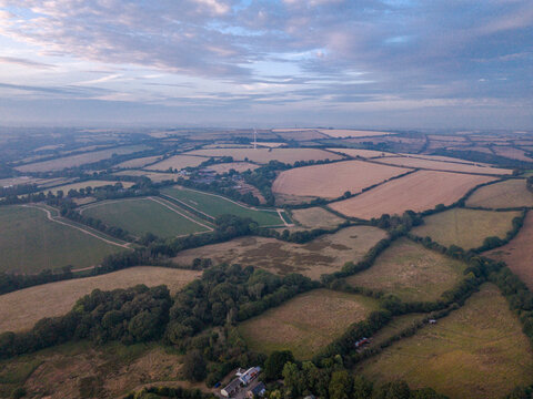 Aerial view of agricultural farmland with hedgerows, tracks, and freshly harvested fields in the rural landscape of Looe, Cornwall, United Kingdom.