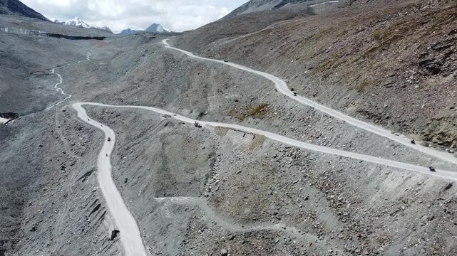 Aerial View of Serpentine Road in Remote Himalayan Mountains with Snow-Capped Peaks and Rocky Terrain, Clear Sky, Daytime Shot