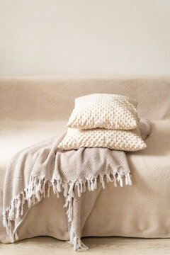 Textured decorative pillows in milky-beige hue, stacked atop patterned throw blanket with white fringe, resting on beige sofa against neutral backdrop. Quiet luxury, cozy home accessories