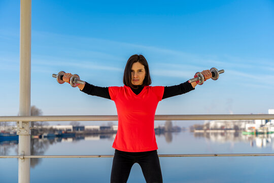 Woman performing shoulder workout with dumbbells outdoors, focusing on strength and fitness