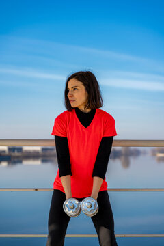 Woman exercising holding dumbbells by the river, focusing on her outdoor workout