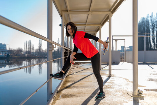 Young woman working out with a dumbbell, performing triceps extensions outdoors on a pier