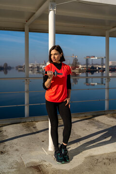 Woman performing a bicep curl with a dumbbell outdoors, focusing on her workout along waterfront