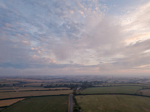Aerial view of the misty rural countryside near Looe, featuring foggy fields, agricultural farmland, and a winding country road in Looe, Cornwall, United Kingdom.