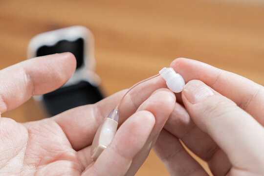 A pair of hands holds a modern digital hearing aid device, highlighting careful maintenance and routine care for personal wellness within a healthcare context to improve auditory health