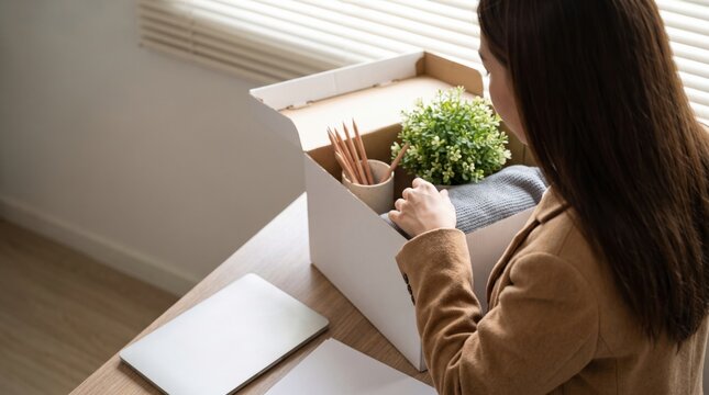 Woman packing personal belongings into a cardboard box after job loss or resignation from office.