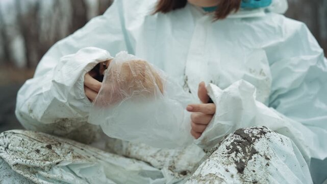 Caucasian scientist in white protective suit sitting on muddy abandoned street tearing ration bread, hands dirty and numb from frost, overcast winter forest backdrop, isolated survivor scene conveying