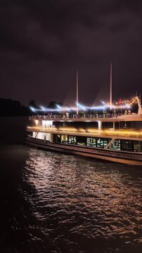 Eye level view of illuminated cruise ship sailing on dark water at night in Ha Long Bay, Vietnam
