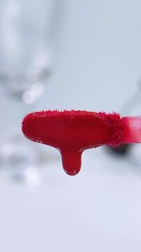 Close up of a red brush isolated on soft white background dripping red liquid. Beauty cosmetic tool for makeup application concept.