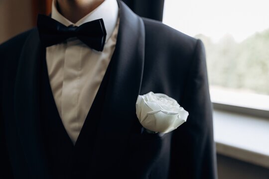 Elegant groom wearing a dark suit with a black bow tie and a white rose boutonniere pinned to his lapel.
