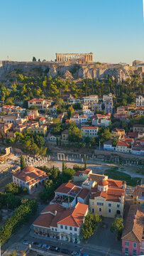 Aerial view of the Acropolis of Athens with the Parthenon standing atop the rocky hill overlooking the historic Plaka neighborhood with its terracotta rooftops and narrow streets in Greece.