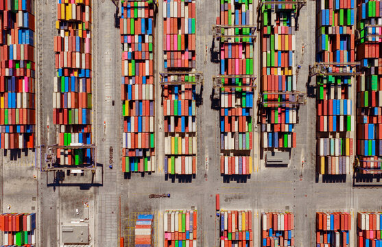 Aerial view of colorful shipping containers stacked in rows at a busy port terminal in Greece.