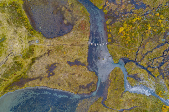 Aerial view of the Slettvikane landscape featuring a winding river with stepping stones crossing the water, surrounded by mossy terrain and autumn vegetation in Fjord, More og Romsdal, Norway.