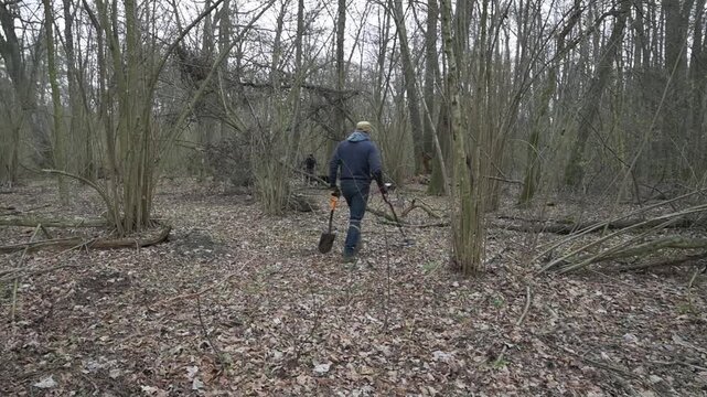 Treasure Hunter Searching with Metal Detector and Shovel in an Overgrown Forest Landscape