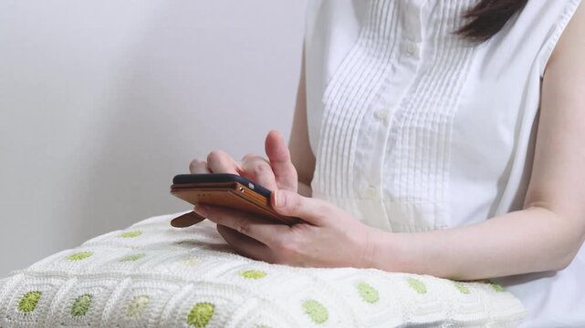 クッションを膝に乗せてくつろいでスマートフォンを操作する人の手元