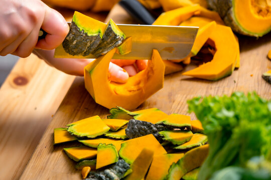 Cooking autumn food &mdash; hands slicing raw pumpkin with cleaver knife on wooden board. Comfort home cooking process with fresh organic ingredients. Healthy eating culinary concept for food blog.
