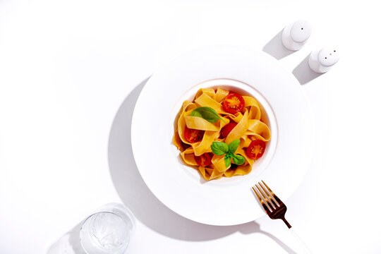 Fresh pasta - Italian food with tomato and basil. Table setting with clear pure water and golden fork. Mindful eating wellness trend. Traditional carbohydrate lunch promoting modern healthy lifestyle.