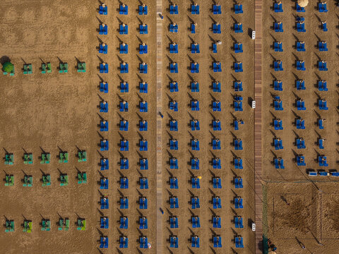 Aerial view of rows of blue sun loungers and umbrellas arranged on the sandy beach of Cervia, Emilia-Romagna, Italy.