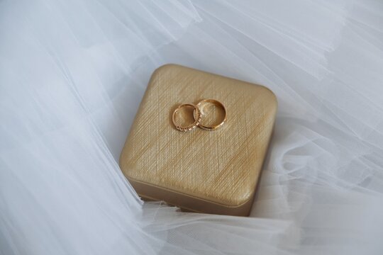 Close up of two gold wedding rings resting on a small wooden ring box enveloped in soft white tulle.