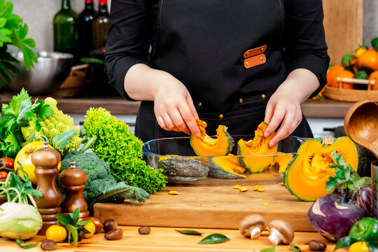 Comfort food cooking &mdash; chef hands placing pumpkin in glass baking dish. Homemade vegetarian autumn dinner preparation. High culinary art with organic seasonal vegetables on wooden table.