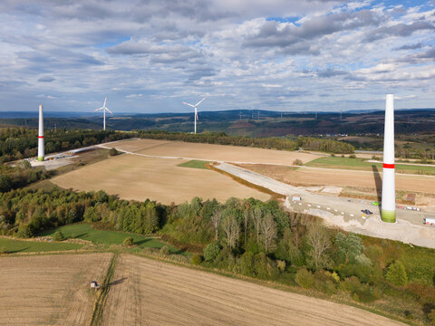 Aerial view of a wind turbine construction site featuring partially erected turbines in a rural landscape with agricultural fields and forests in Trier, Rhineland-Palatinate, Germany.