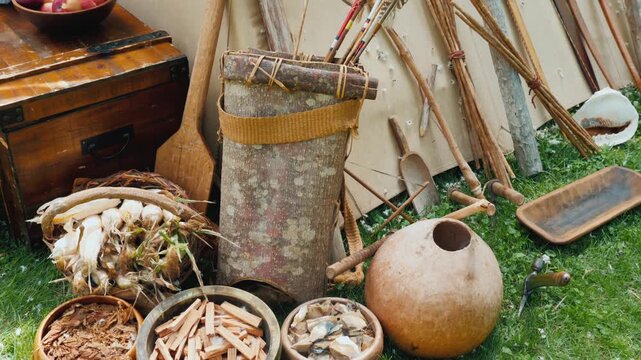 Native american historical reenactment display of primitive tools weapons and supplies arranged on grass.