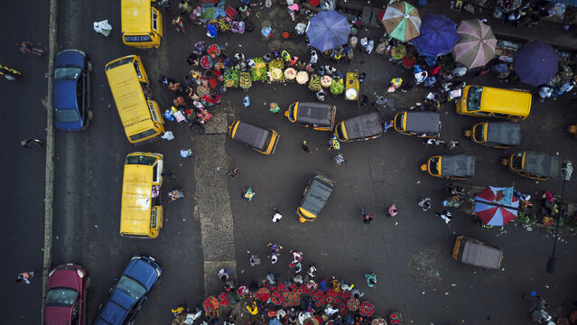 Aerial view of the bustling Agege market featuring numerous yellow buses, colorful umbrellas, and people navigating the busy streets of Lagos, Lagos, Nigeria.