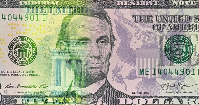 Five Dollar Bill Under Moving Green Security Light. Five dollar bill security light scans across Lincoln portrait. Green illumination shifts over printed details during smooth currency inspection.