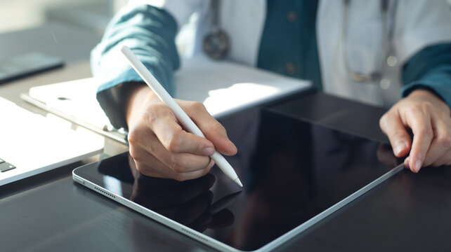 Doctor using stylus pen and digital tablet for electronic health records, examining patient health information, working in doctor's office in modern hospital, closeup. Medical technology