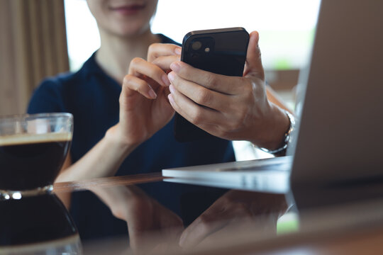 Young asian woman using smartphone with laptop on table during remote work at coffee shop, digital nomad lifestyle, online business concept