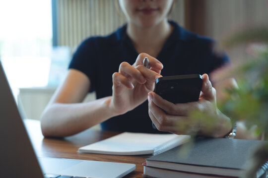 Woman using smartphone searching and browsing the internet with laptop on table, remote working at cafe modern workspace