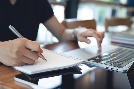 Business woman searching the information on laptop and taking note in notebook, working at modern workspace