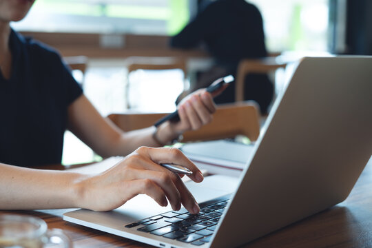 Woman working on laptop and using smartphone, browsing the internet at coffee shop, freelance at work, online business concept