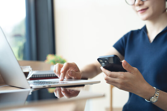 Woman freelancer using smartphone during working on laptop at modern workspace, online business, remote work concept