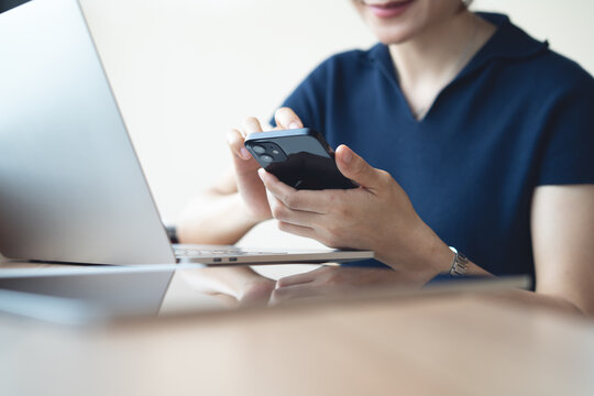Woman using smartphone for online messaging during working at cafe or home office with laptop on table, remote work, online business concept
