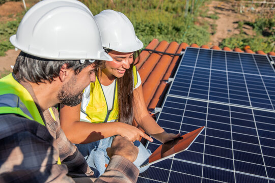 Multicultural solar engineers discussing installation of solar panels on rooftop