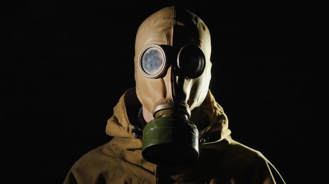 Person wearing vintage soviet gas mask in dark studio standing still while breathing heavily for cinematic effect.