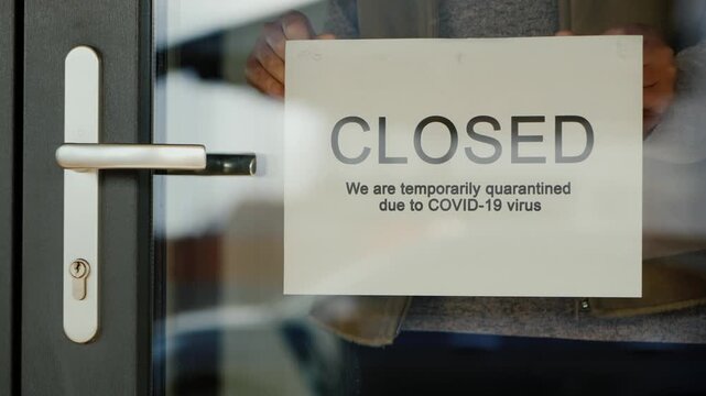 Woman hands hang a paper sign with the text closed due to covid-19 virus on the glass door, small business during pandemic.