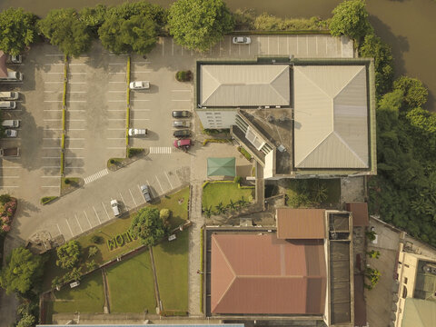 Aerial view of the University of Lagos campus featuring academic buildings, a large parking lot with parked cars, and lush green lawns situated along the waterfront in Lagos, Lagos, Nigeria.