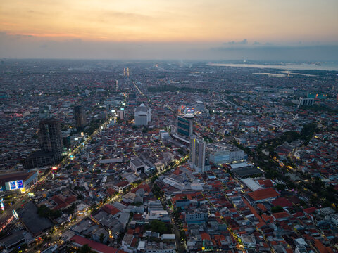 Surabaya, Indonesia - 28 August 2026: Aerial view of the urban landscape of Surabaya at sunset, with dense residential rooftops, high-rise buildings, and glowing city lights.