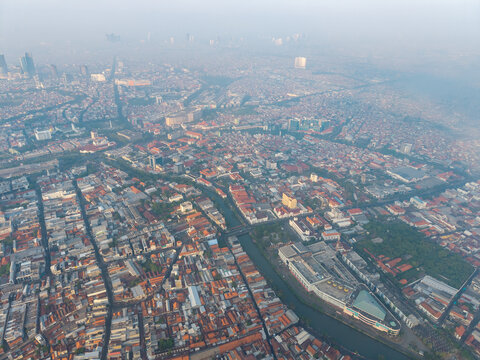 Genteng, East Java, Indonesia - 13 August 2026: Aerial view of Surabaya Old Town featuring dense historic rooftops, a central canal, and urban infrastructure under a hazy sky.