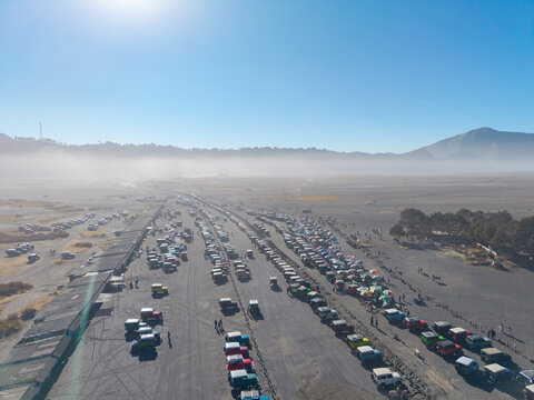 Tosari, East Java, Indonesia - 07 August 2026: Aerial view of tourist jeep cars parked on the volcanic sand plains of Mount Bromo, with misty mountains in the background.